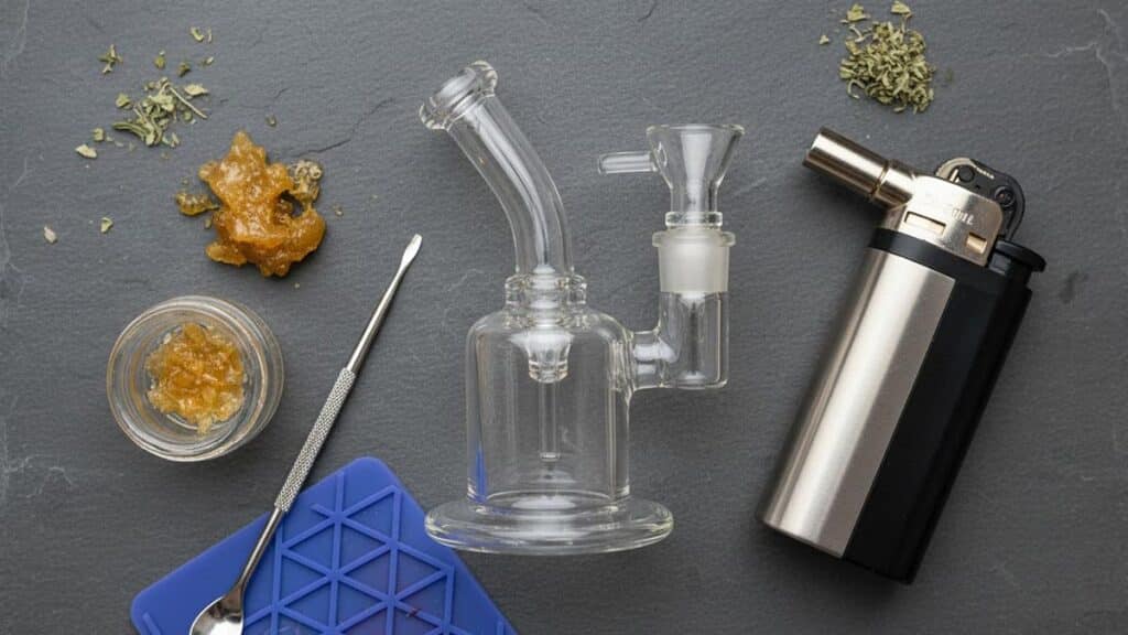 A top-down view of dabbing equipment, including a glass rig, concentrate, dab tool, and torch lighter.